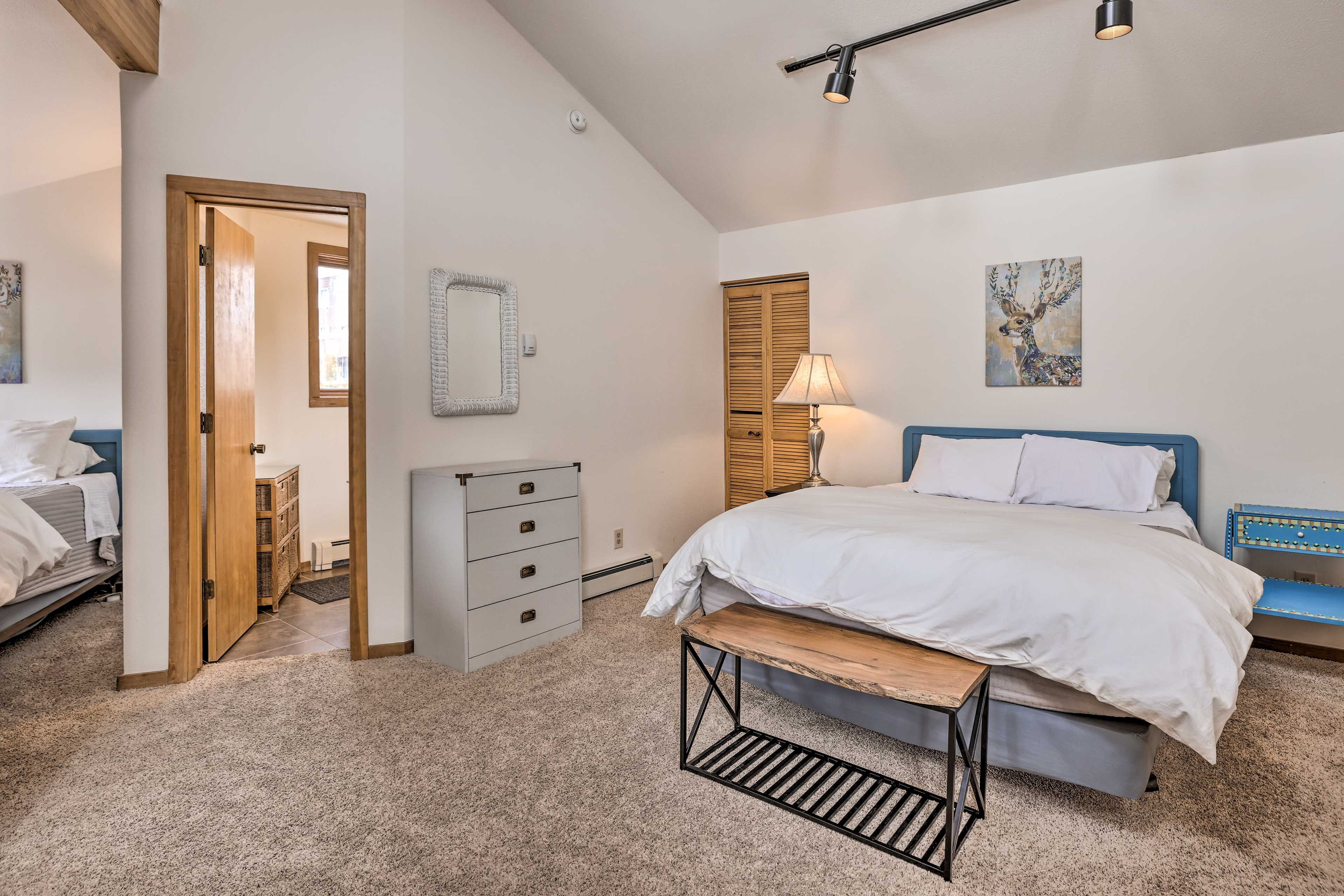 A bedroom with a bed, bedside table, dresser, and a door leading to another room.