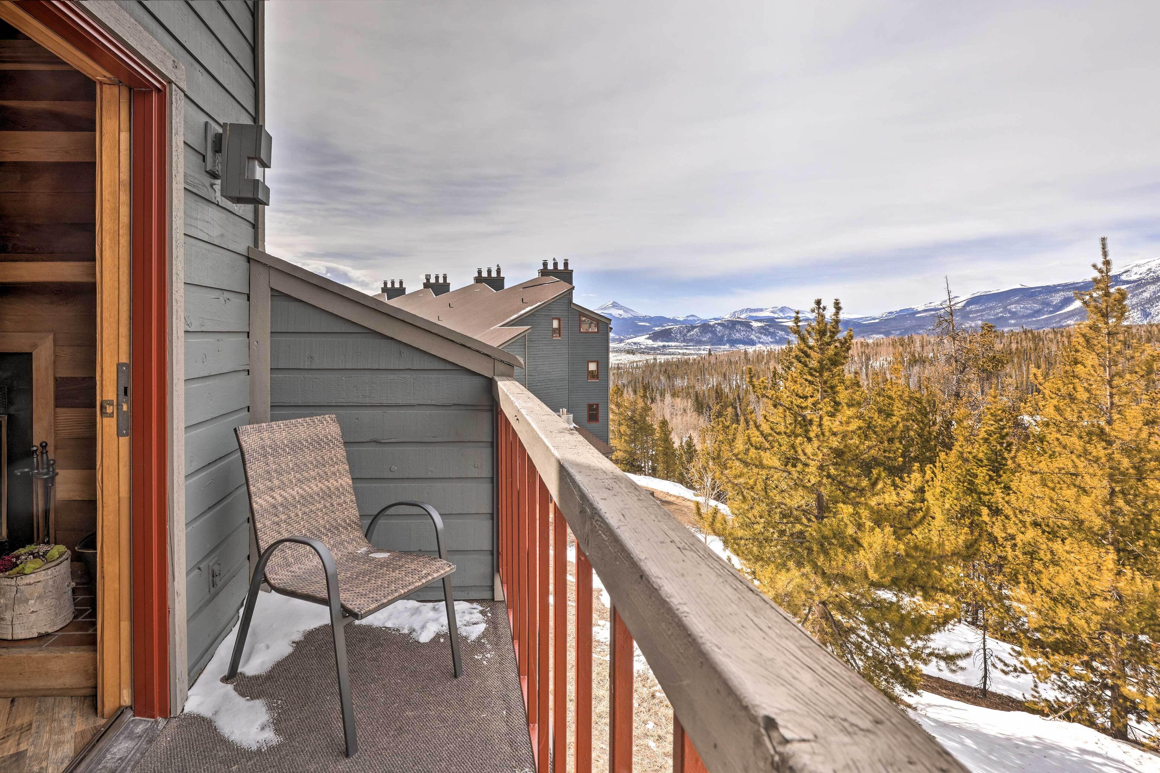 A balcony with a chair, a wooden railing, and a view of a forest and mountains.
