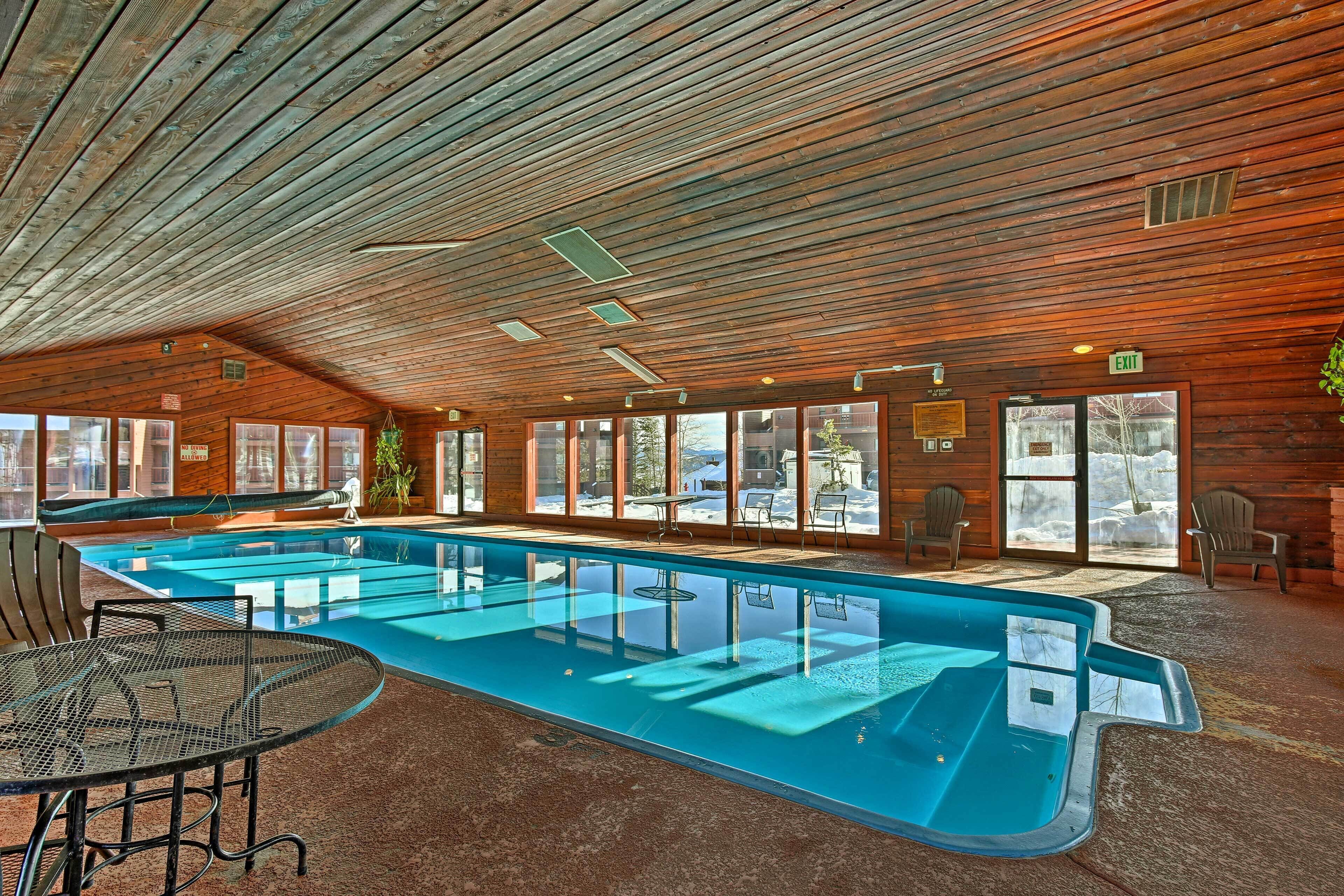 A pool area with a glass-enclosed pool, wooden ceiling, and seating by the pool.