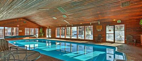 A pool area with a glass-enclosed pool, wooden ceiling, and seating by the pool.
