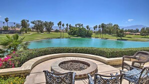Piscina con fogata y mobiliario exterior, rodeada de vegetación y palmeras, con un campo de golf y montañas al fondo.