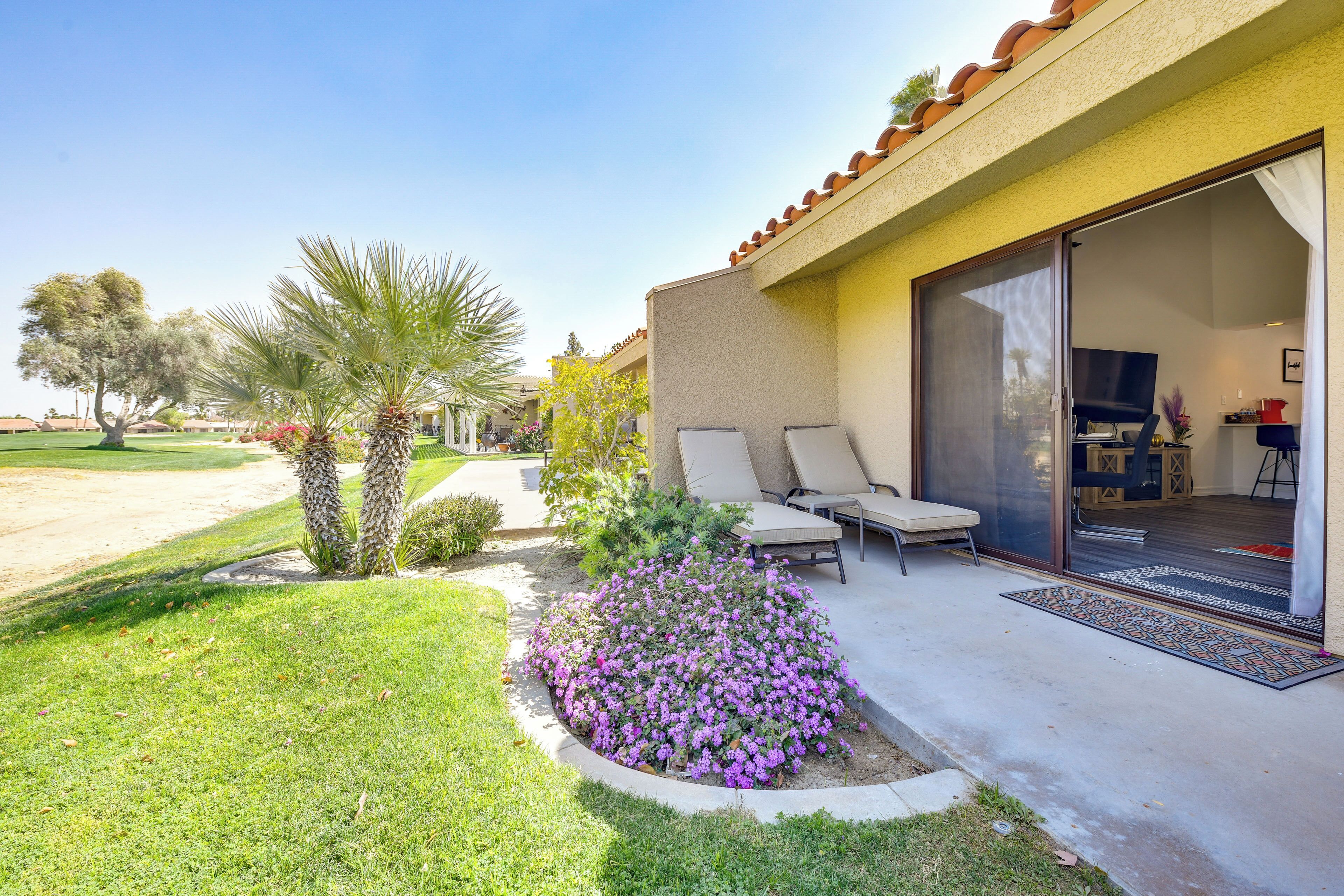 A residential property with a patio, outdoor seating, and a garden with purple flowers.