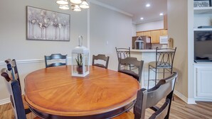 A dining area with a round wooden table, six chairs, a white lantern, and a painting on the wall.