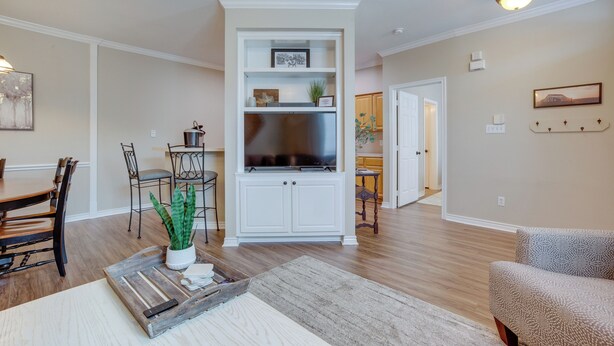 A living room with a TV, white cabinetry, a dining area with a table and chairs, and a kitchen in the background.