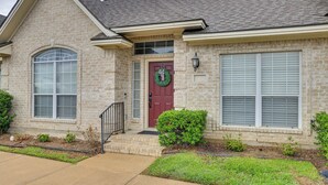 A two-story house with a brick facade, a red front door, and a green wreath.