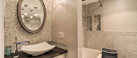 A bathroom with a white sink, a mirror, a mosaic-tiled wall, and a bathtub.