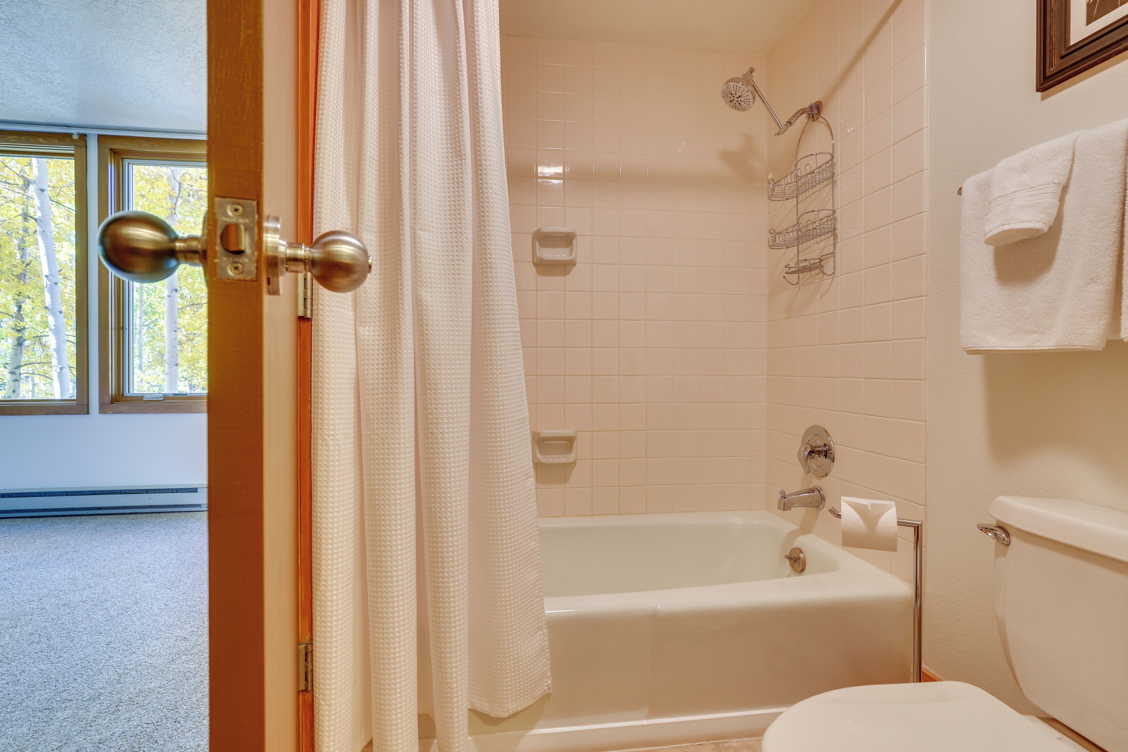 A bathroom with a bathtub, toilet, and a window with a view of trees.