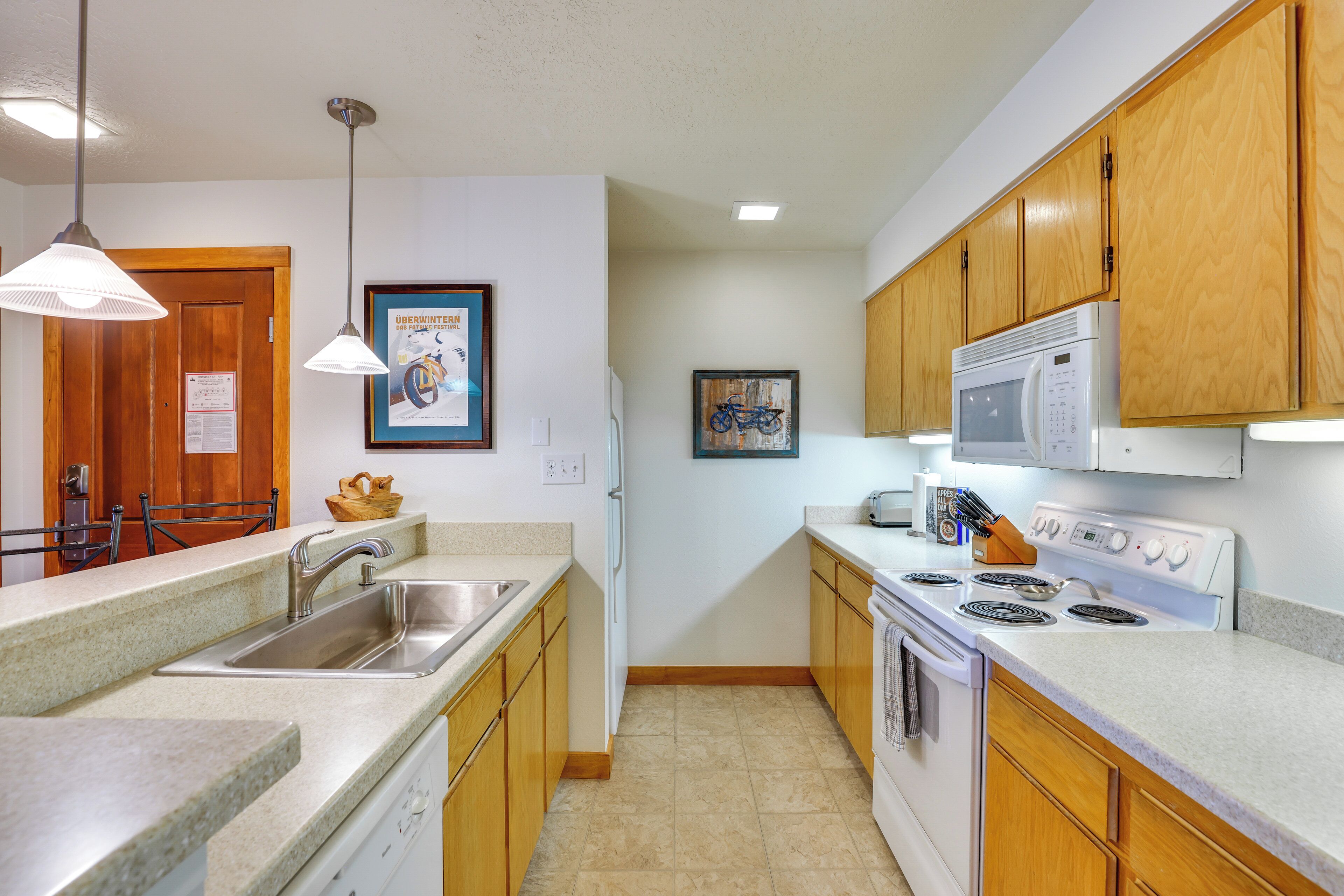 A kitchen with wooden cabinets, a stainless steel sink, a microwave, and a stove.