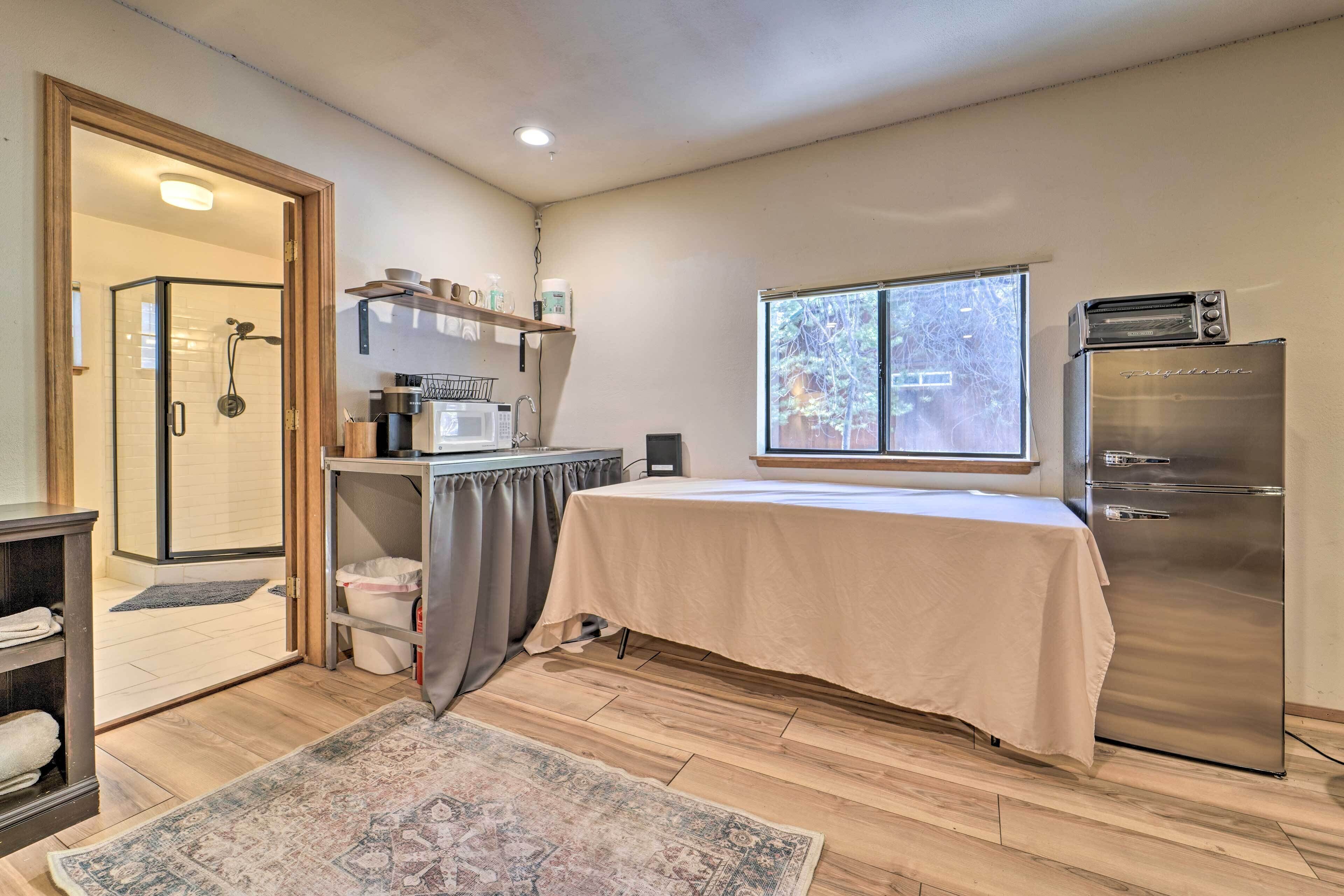 A compact kitchen with a microwave, toaster, and refrigerator. There's a small dining area with a table and chairs, and a shower area with a glass door.
