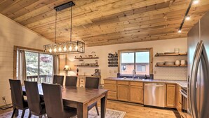 A modern kitchen with wooden cabinets, a stainless steel refrigerator, and a dining area with a wooden table and chairs. - Game Room: Mountain Chalet 5 Mi to Donner Lake (Truckee)