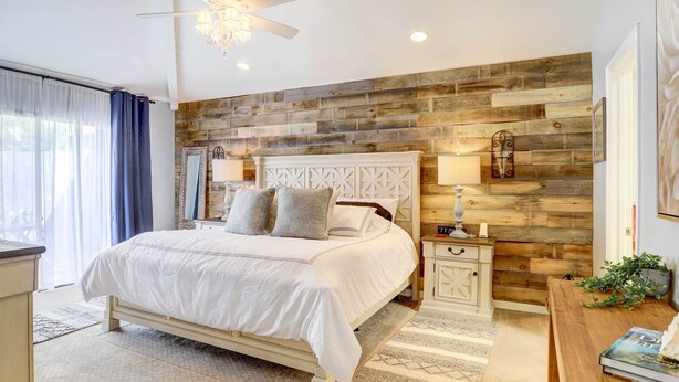 Une chambre avec un mur d’accent en bois, un lit blanc, des tables de chevet et un ventilateur de plafond.