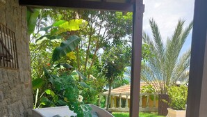 Un área de comedor al aire libre techada con una mesa dispuesta para dos personas, rodeada de plantas tropicales y vistas a un edificio tradicional.