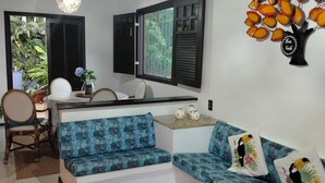 Una habitación con sofá, una mesa de comedor, sillas, un tapete azul, una lámpara colgante y un adorno en la pared.