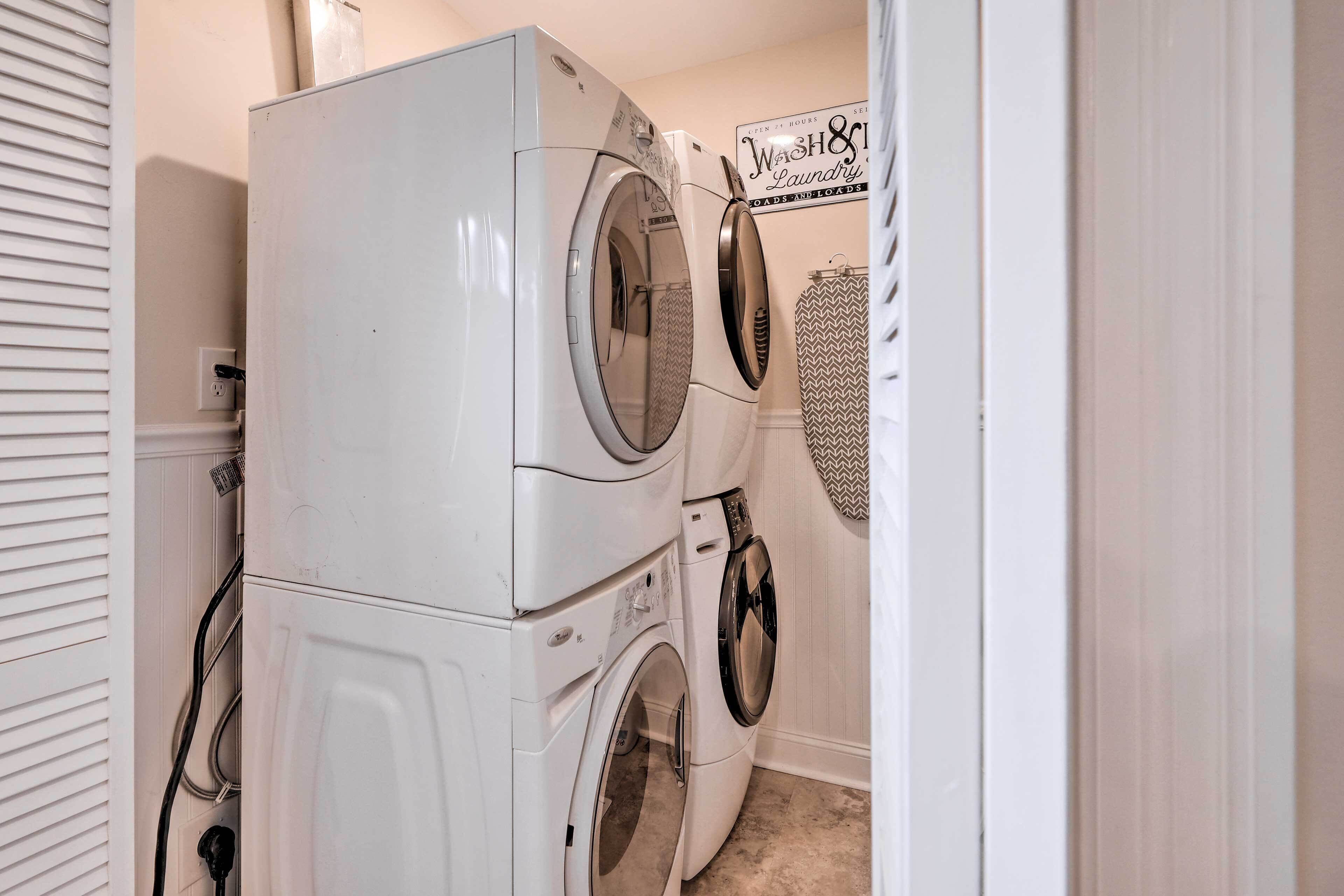 A laundry room with stacked front-loading washers and dryers, a sign indicating 24-hour service, and a patterned shower curtain.