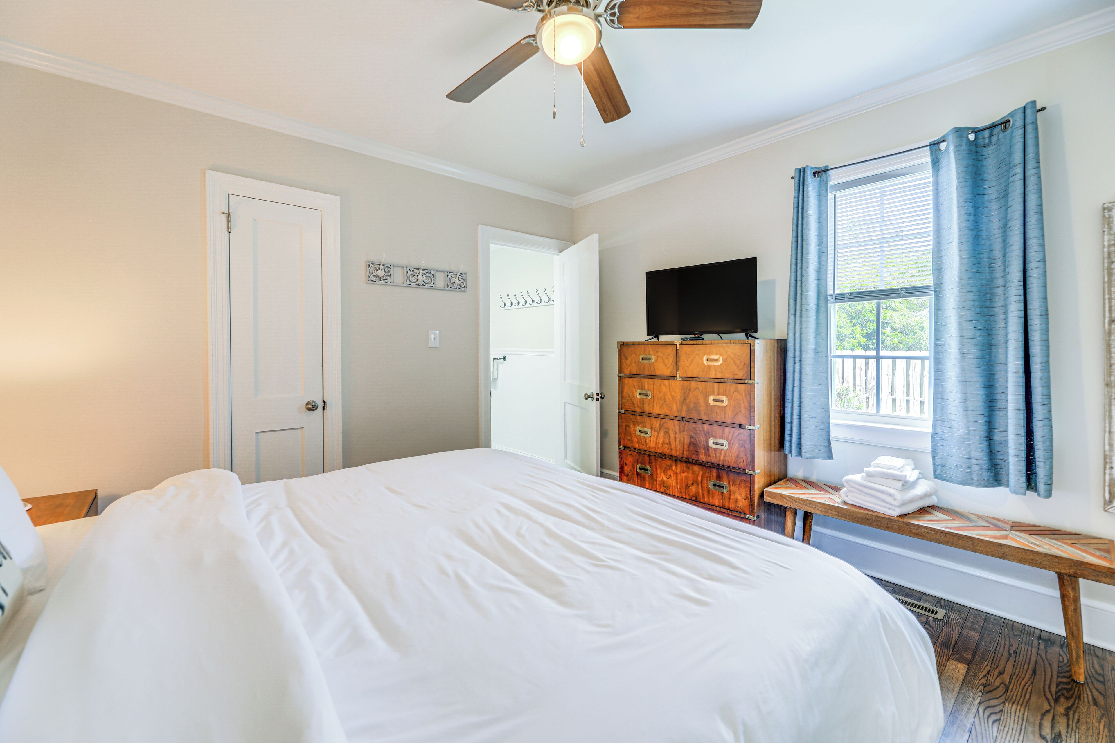 A bedroom with a bed, a dresser, a ceiling fan, a TV, and a window with curtains.