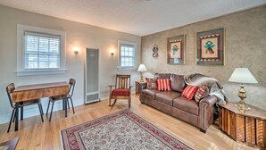 A living room with a wooden dining table, two chairs, a brown leather sofa, a red and white patterned rug, and two wall-mounted lamps. - Well-equipped Cody Cottage: 2 Mi to Cody Rodeo! (Cody)