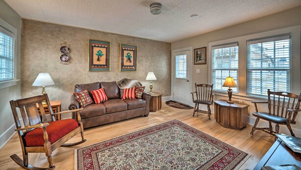 A living room with a brown leather sofa, a rocking chair, and a wooden coffee table. There are two lamps on side tables, and a patterned rug on the floor. - Well-equipped Cody Cottage: 2 Mi to Cody Rodeo! (Cody)