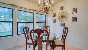 Un coin repas avec une table en verre entourée de chaises en bois, un lustre et des tableaux encadrés accrochés au mur.