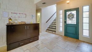 Un hall d’entrée spacieux, agrémenté d’un meuble en bois foncé, d’une porte de couleur turquoise ornée de motifs en verre et d’un escalier dont les marches sont recouvertes de carreaux décoratifs.