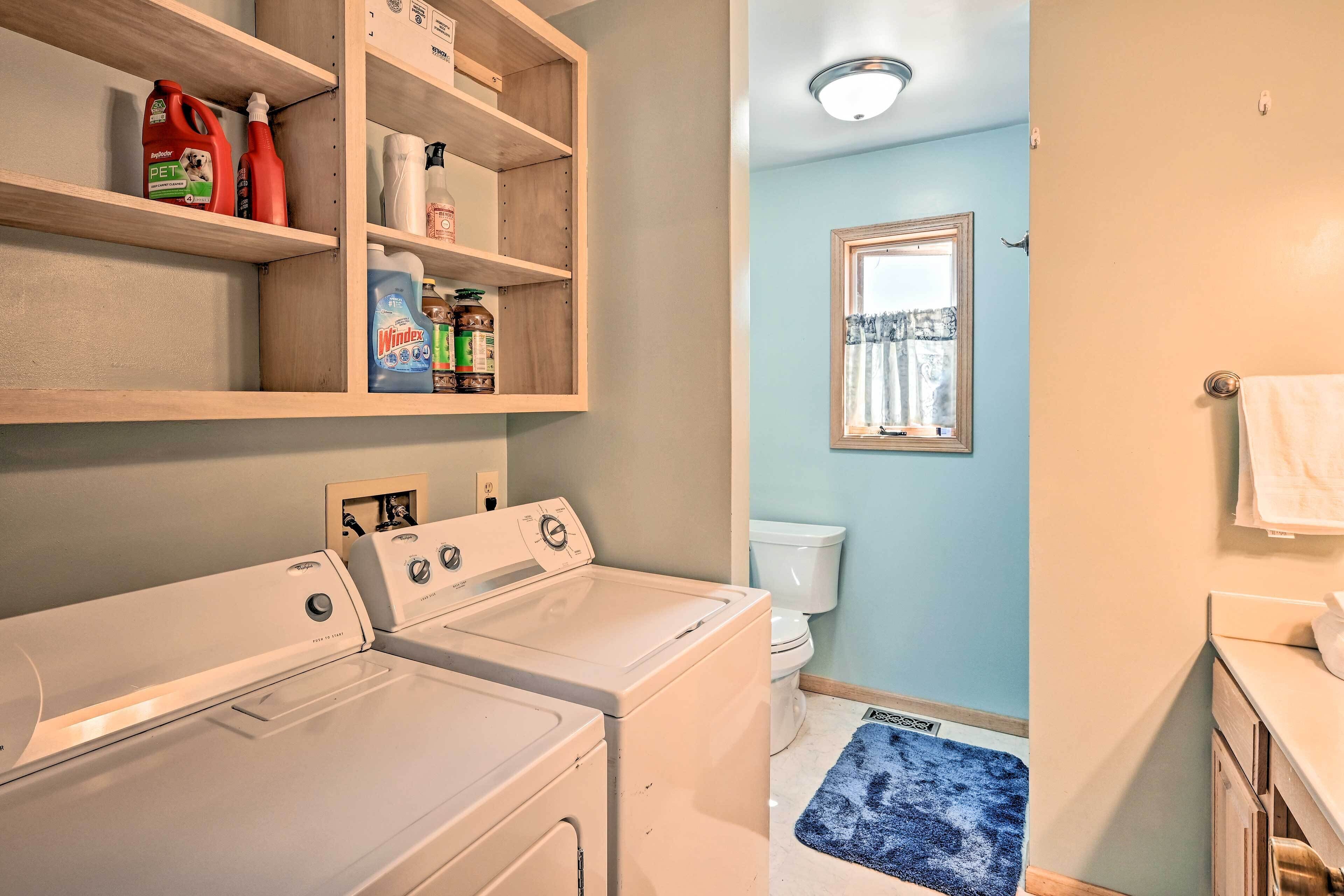 A laundry area with two white washers and dryers, shelves with cleaning supplies, a toilet, and a blue rug.