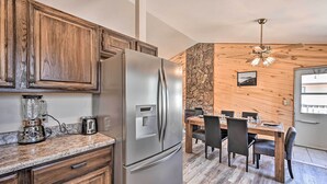 A modern kitchen with wooden cabinets, a stainless steel refrigerator, a granite countertop, a dining area with a wooden table and chairs, and a ceiling fan. - Charming Buena Vista Home w/ Hot Tub + Deck! (Buena Vista)