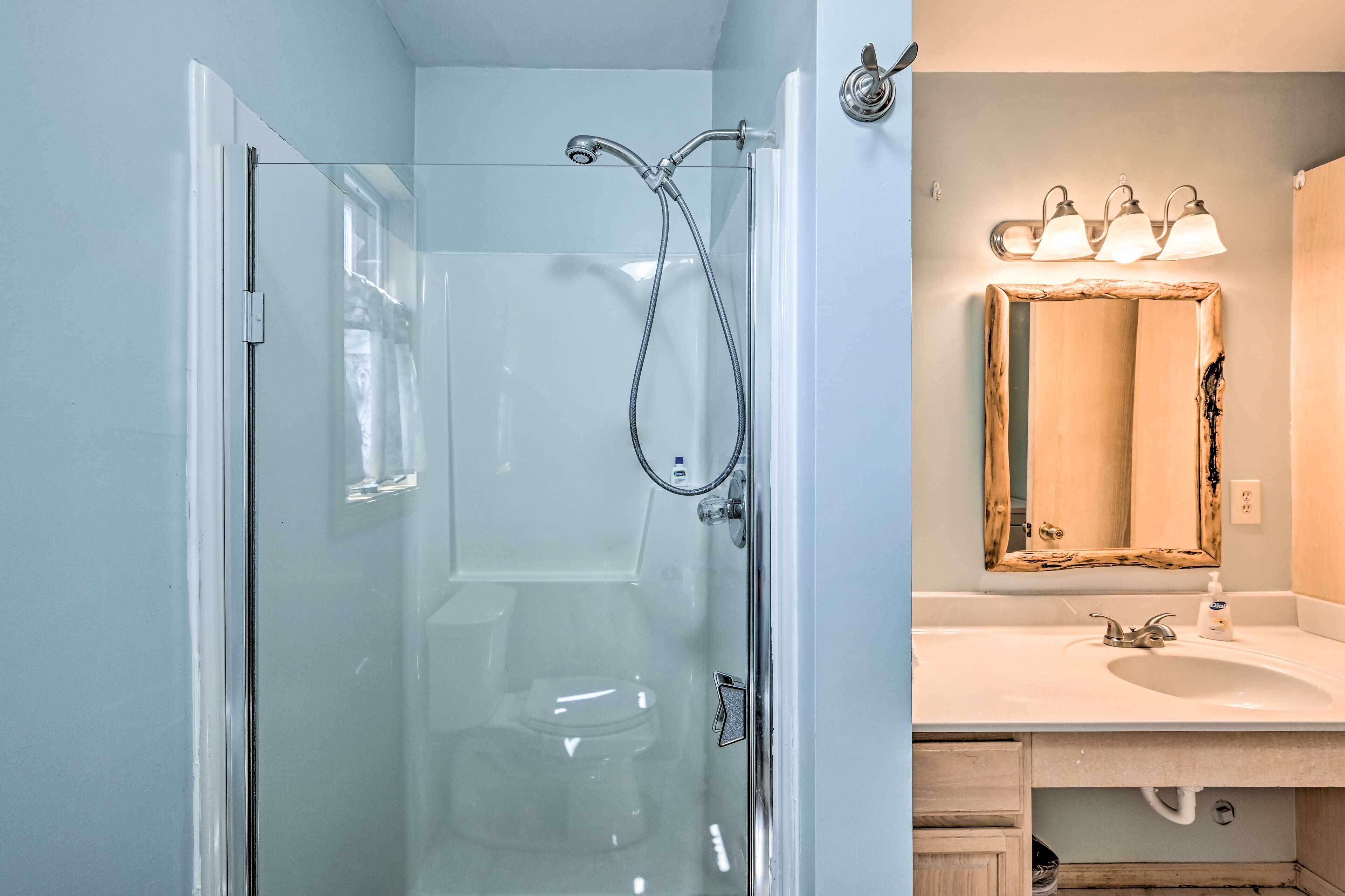 A bathroom with a glass-enclosed shower, a white sink, and a mirror with three lights.