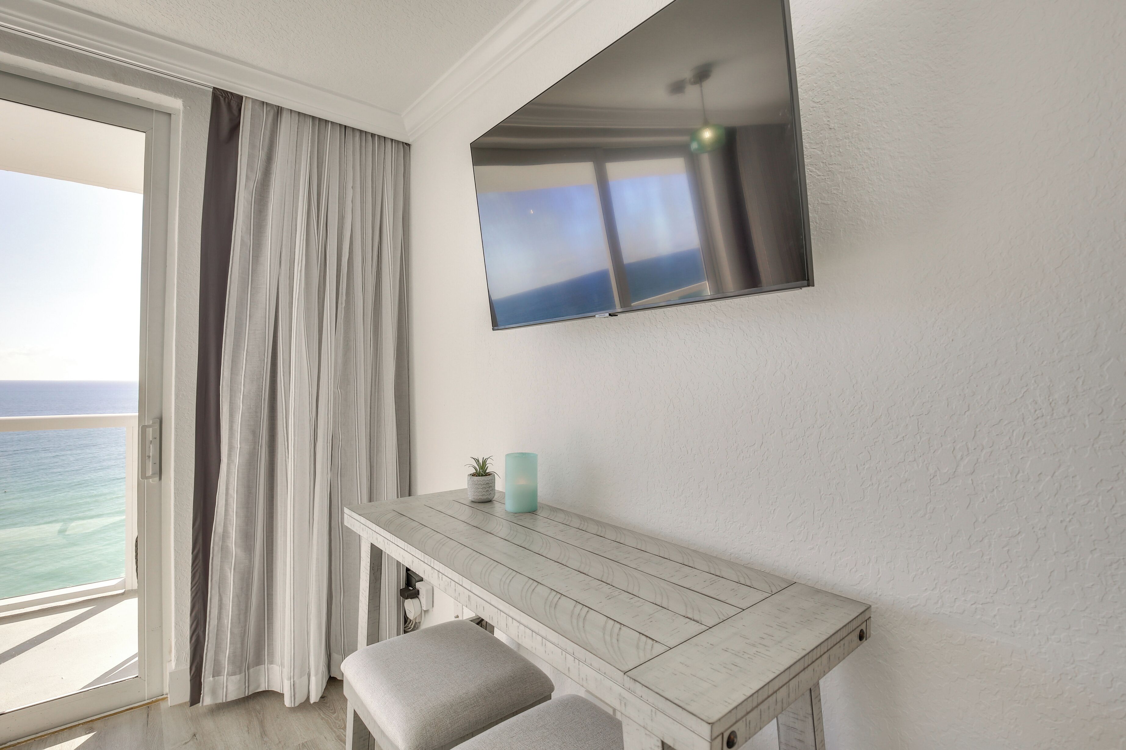 Una habitación con un ventanal grande, un televisor de pantalla plana en la pared, una mesa de madera y un banco.