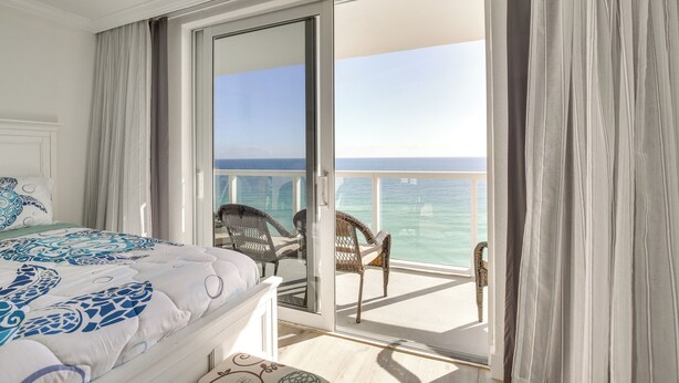 Une chambre avec un lit, un balcon donnant sur la mer et un fauteuil.