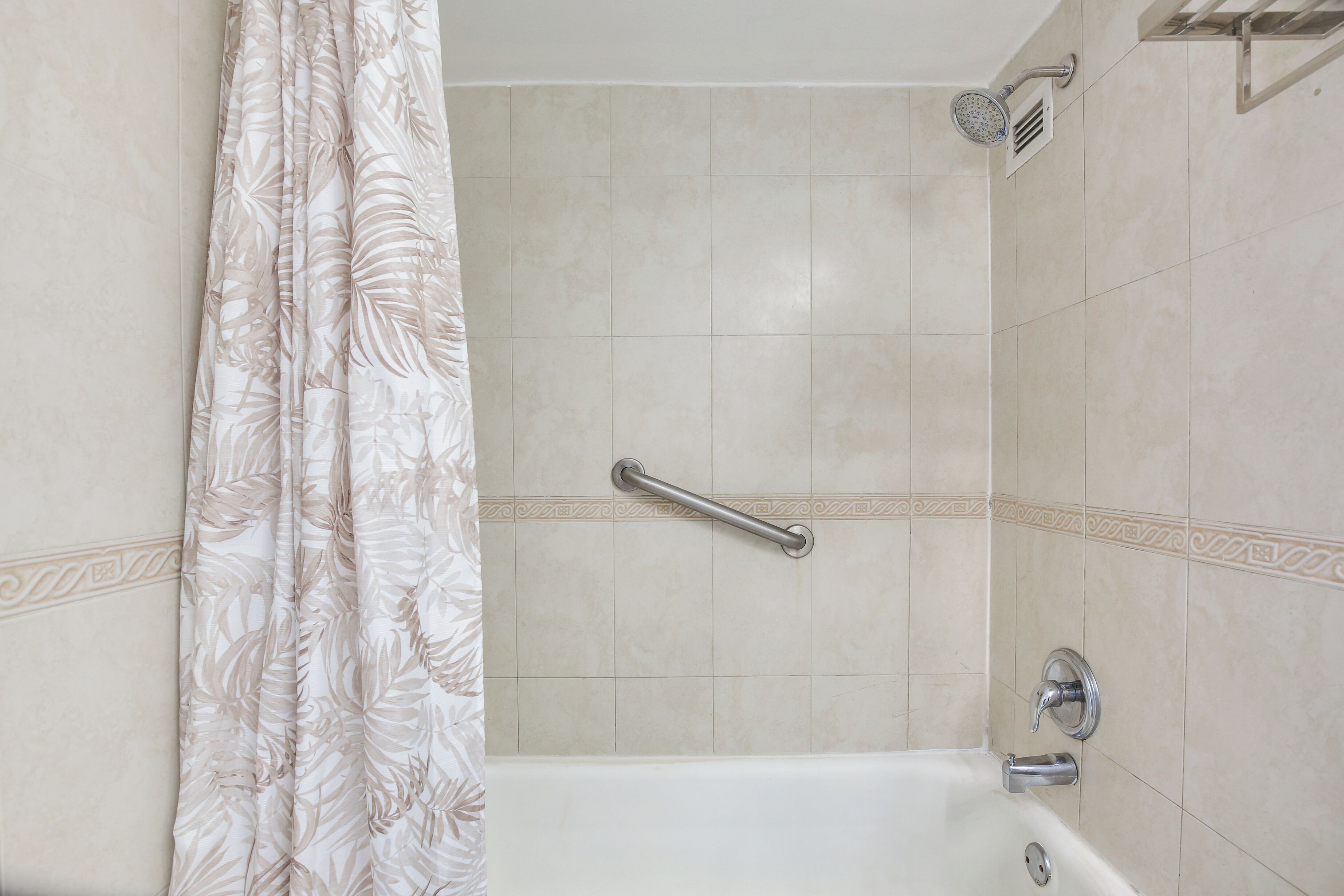 Un baño con bañera, cabezal de ducha y barra de apoyo.