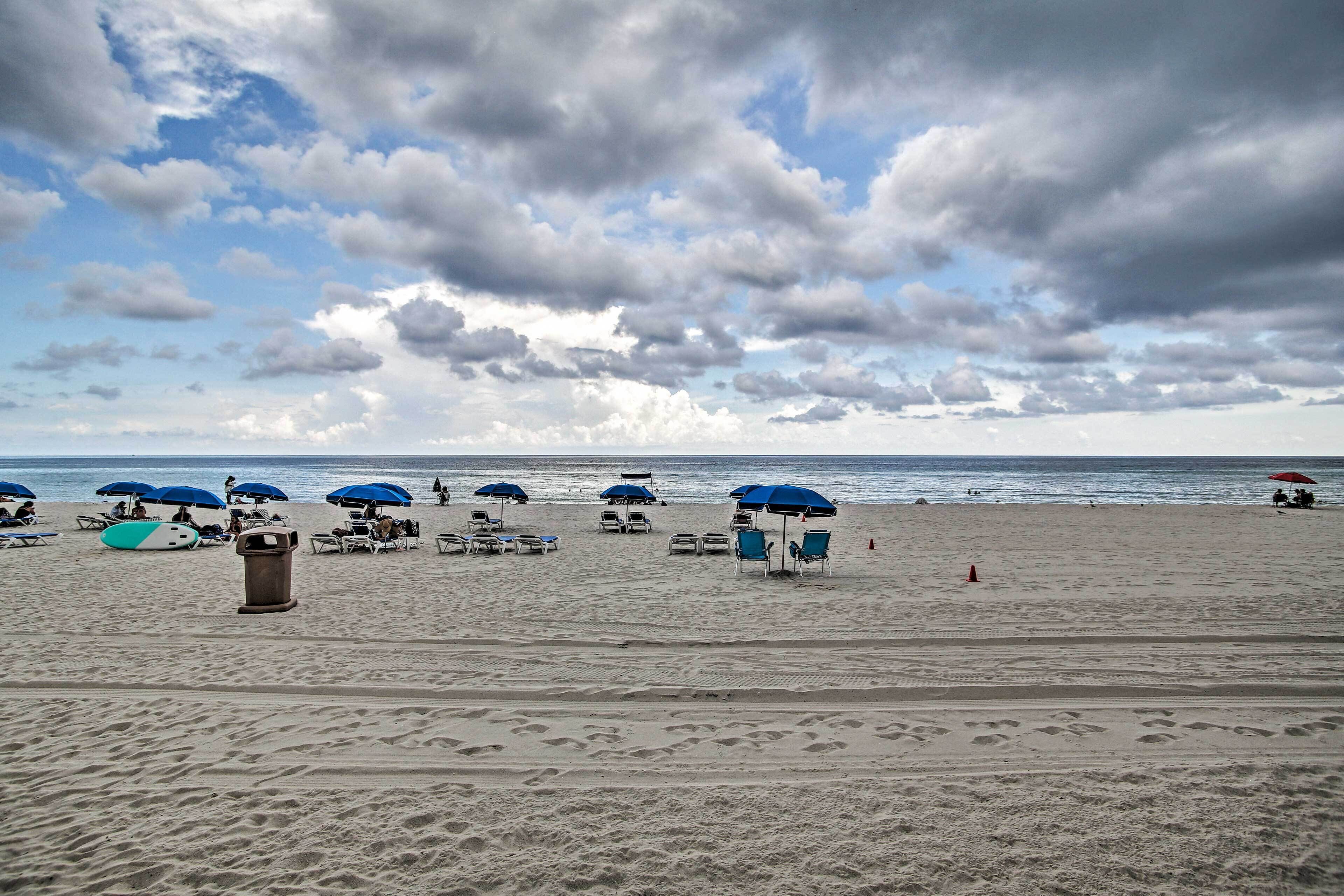 A beach with umbrellas, lounge chairs, and a trash can.