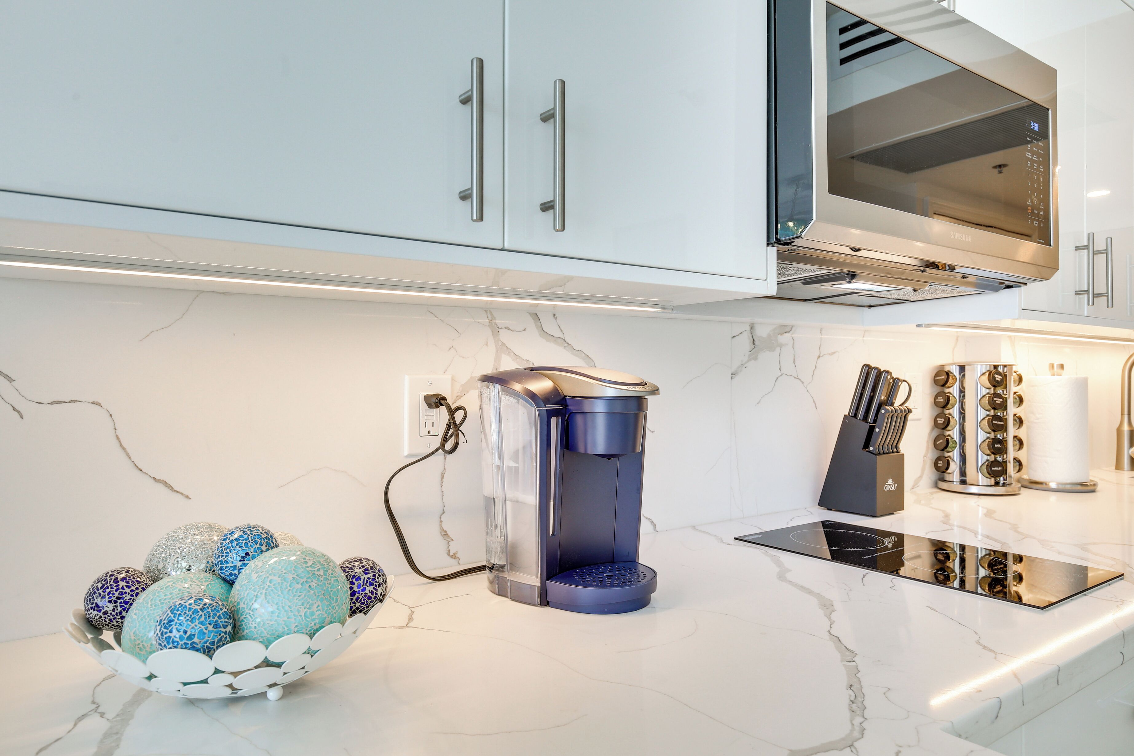 A modern kitchen with white cabinets, a built-in microwave, a coffee maker, and a knife block.