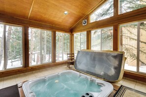 Eine Holzhütte mit Whirlpool, großen Fenstern und Blick auf Bäume.