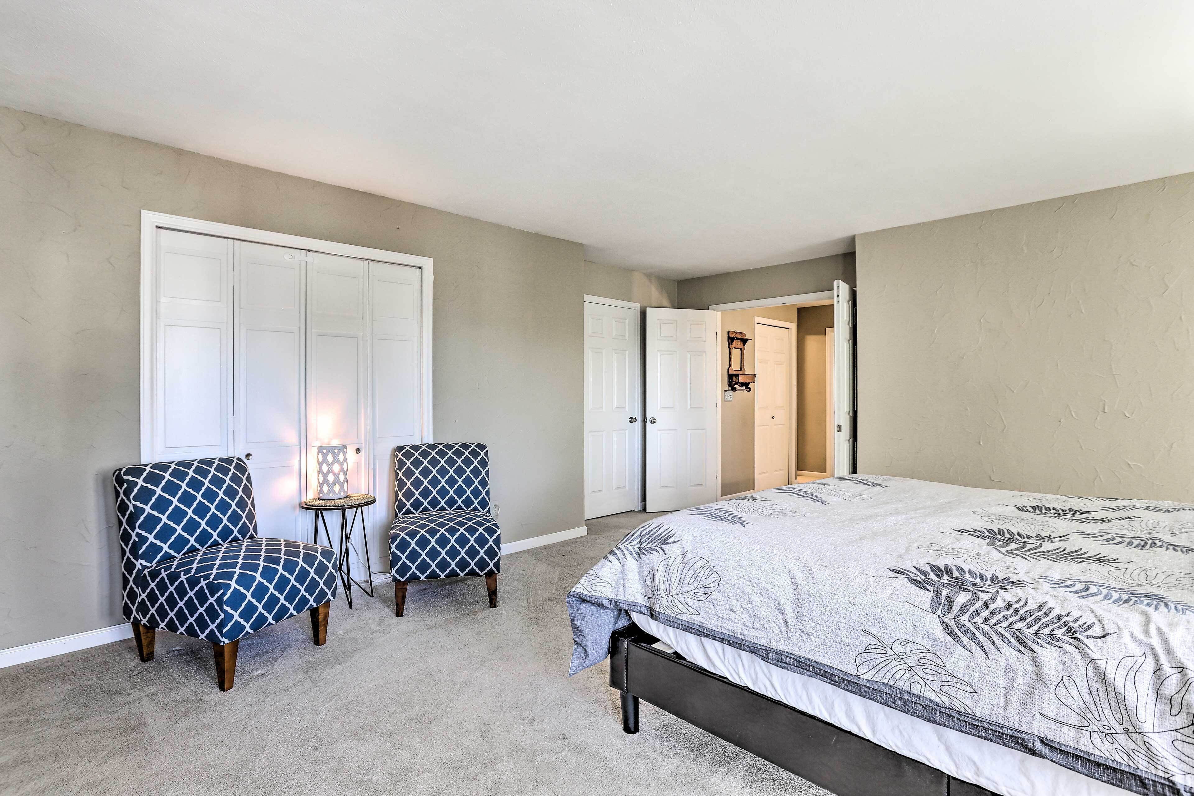 A bedroom with a bed, two matching chairs, a small table, and a closet.
