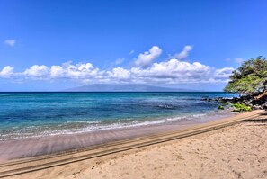 Una playa con aguas azul cristalino, una orilla de arena y una montaña al fondo.