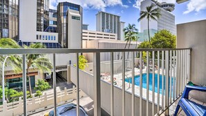 A balcony with a view of a swimming pool, high-rise buildings, and palm trees. - Centrally Located Vacation Rental in Waikiki! (Honolulu)