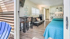 A cozy room with a sofa, a small table, a blue chair, a bed with a blue blanket, and a kitchen area in the background. - Centrally Located Vacation Rental in Waikiki! (Honolulu)