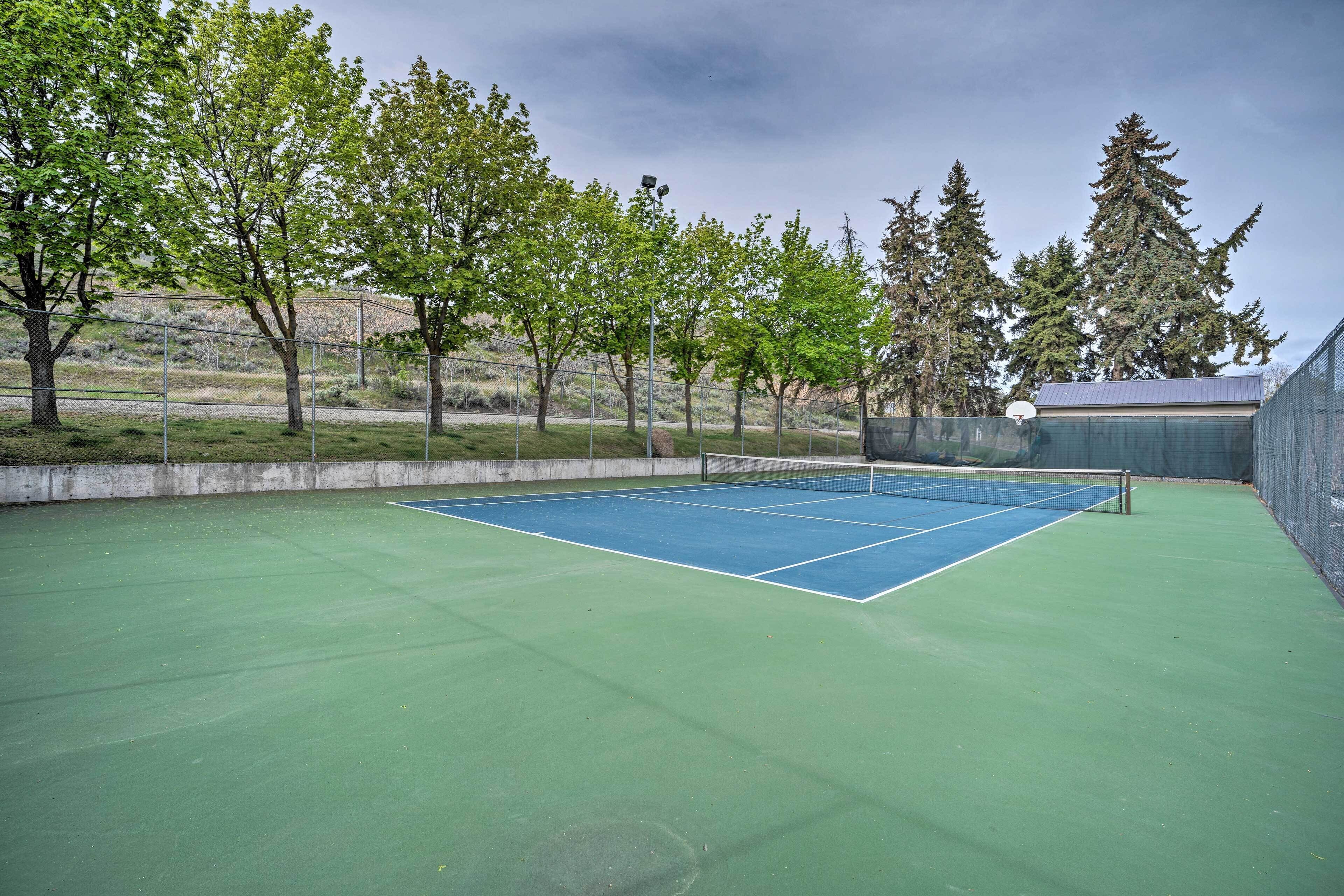 Ein Tennisplatz im Freien mit Netz, umgeben von Bäumen und einem Zaun.