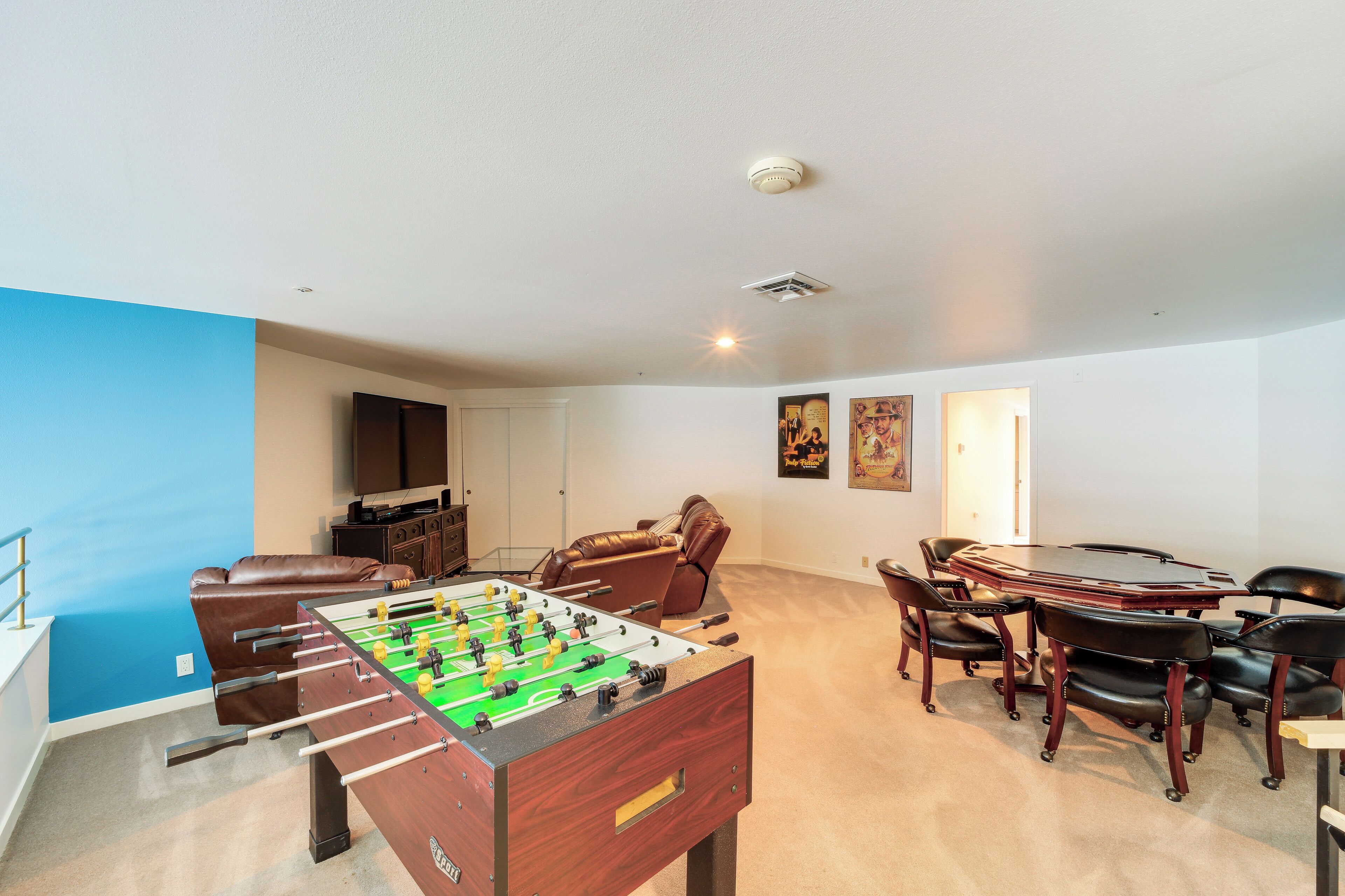 Una habitación con mesa de futbolín, sillas de cuero, mesa de comedor y una zona de cocina.