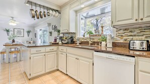 A kitchen with white cabinets, a dishwasher, and a window with a view of trees. - Modern Home in Napa Area w/ Hot Tub & Game Room! (Petaluma)