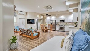 A spacious living area with a sofa, wooden dining table, and chairs, a kitchen with modern appliances, and a ceiling fan.