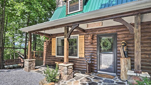 A rustic log cabin with a stone-paved entrance, wooden porch, and a metal door. - Mtn-view Cabin w/ Hot Tub in Sevierville! (Sevierville)
