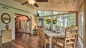 A wooden dining area with a large table and chairs, a ceiling fan, and large windows with a view of trees. - Mtn-view Cabin w/ Hot Tub in Sevierville! (Sevierville)
