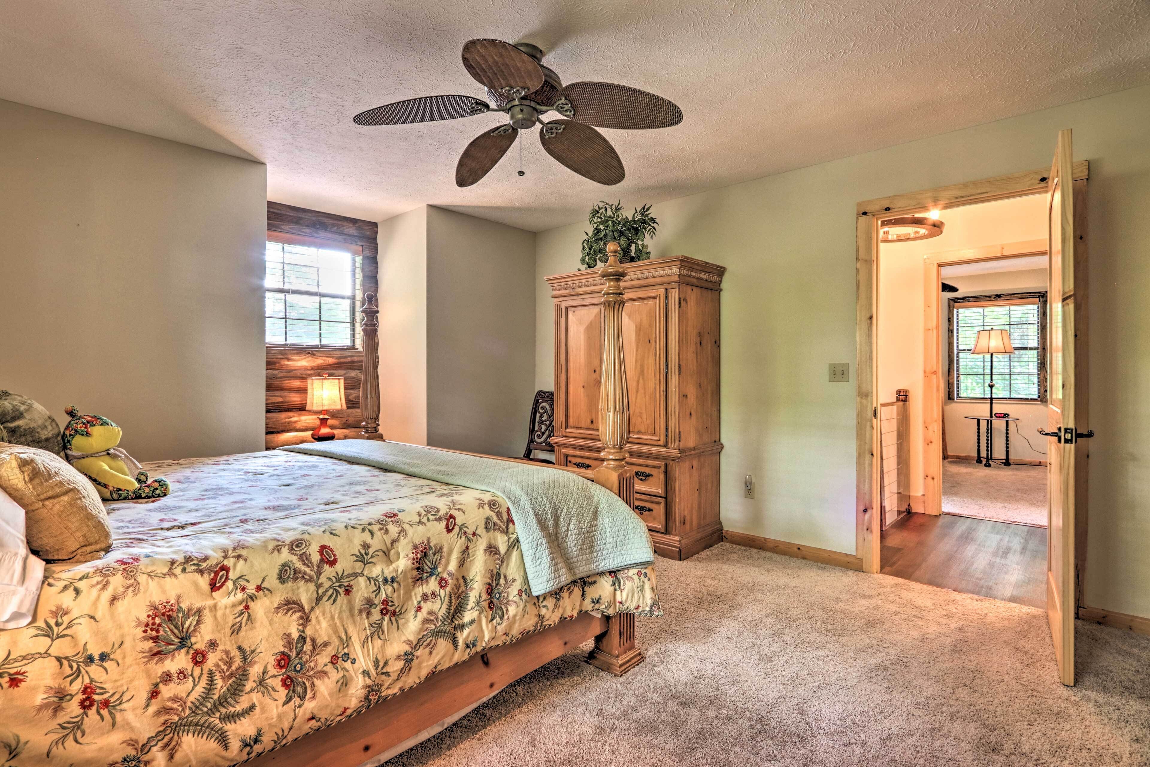 A bedroom with a bed, a wooden wardrobe, a ceiling fan, and a door leading to another room.