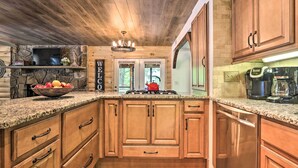A kitchen with wooden cabinets, granite countertops, a stone fireplace, and a 'WELCOME' sign. - Mtn-view Cabin w/ Hot Tub in Sevierville! (Sevierville)
