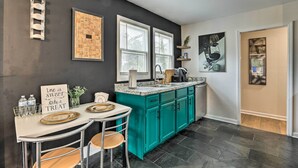 A modern kitchen with teal cabinets, a marble countertop, and a dining area with two chairs and a table set for two. - Charming Atlanta Vacation Home ~ 5 Mi to Dtwn (Atlanta)