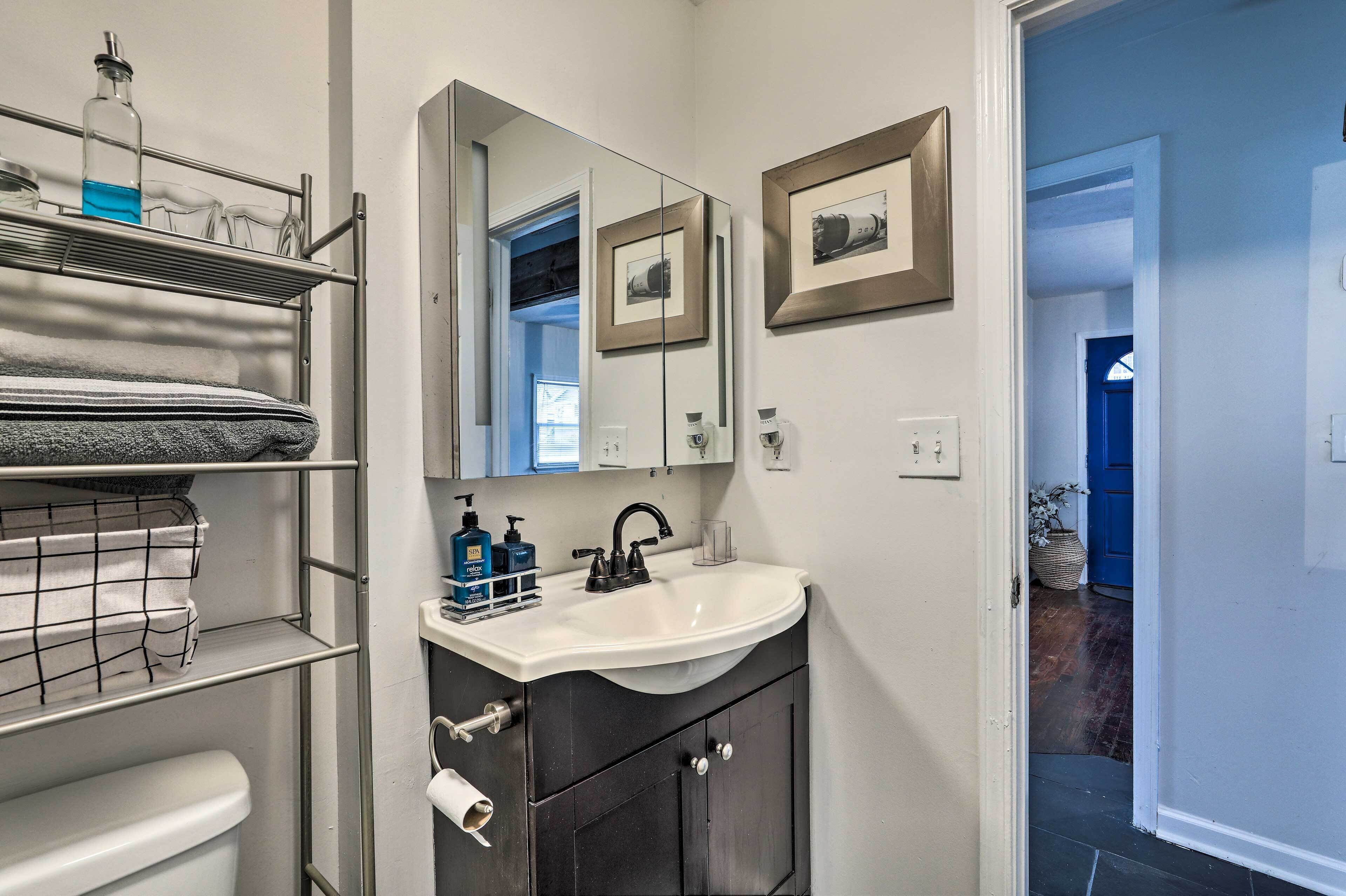 Un baño con lavamanos blanco, muebles oscuros, un perchero y un espejo.