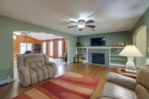 A living room with a fireplace, a ceiling fan, and a large window. - Nature Getaway w/ On-site Trails, 17 Mi to DC! (Brookeville)