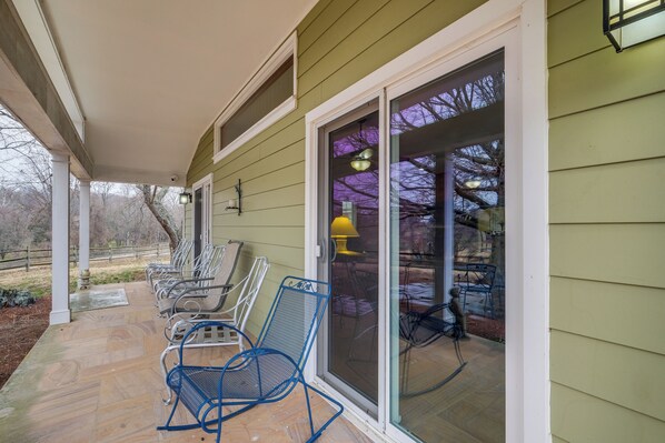 A covered porch with several chairs and a sliding glass door leading to an outdoor area.