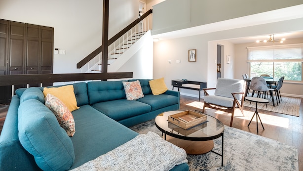 A modern living room with a sectional sofa, a coffee table, and a staircase leading to an upper level. - Modern North Potomac Home w/ Furnished Deck! (Gaithersburg)