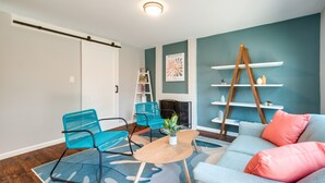 A living room with teal walls, a wooden coffee table, teal and black chairs, a sofa with pink cushions, and a white fireplace. - Modern North Potomac Home w/ Furnished Deck! (Gaithersburg)
